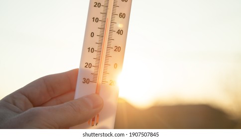 Hand holding thermometer on sky background.