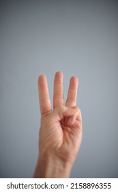 Hand Holding Up Three Fingers Against A Blue Grey Background.