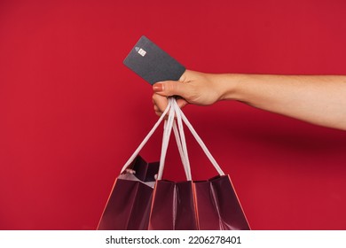 Hand Holding Three Paper Bags And Credit Card In Front Of Red Background.