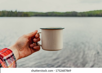 Hand Holding Tin Coffee Cup In Front Of A Lake