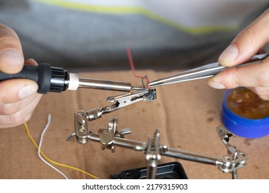 The hand holding the tin, a soldering iron solder the chip in place. a man solders a wire to a microcircuit