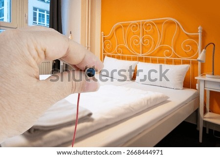 Hand holding tiny spy camera in bedroom setting, Peaceful Sleep in Spacious Bed, unauthorized surveillance, Serene Sleep Haven, Soft Hotel Pillows and Bedding, secrecy stay, security concerns