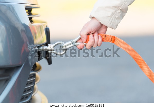Hand holding tow rope near towing hook assembled to a\
broken car
