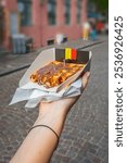 Hand holding a traditional Belgian Liege waffle with chocolate spread, Belgium flag, Belgian street food