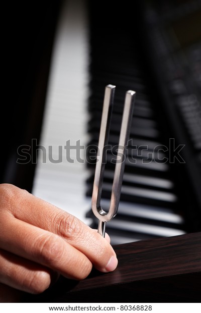 Hand\
holding tuning fork on top of piano wood\
panel