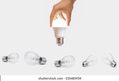 Hand holding a turned on LED light bulb over old incandescent light bulbs / Using economical and environmentally friendly light bulb concept

