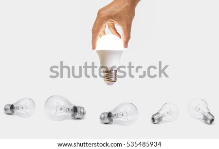 Hand holding a turned on LED light bulb over old incandescent light bulbs / Using economical and environmentally friendly light bulb concept

