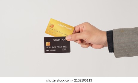 The Hand Is Holding Two Credit Cards And Wearing Suit. Black And Gold Color Cards On White Background.