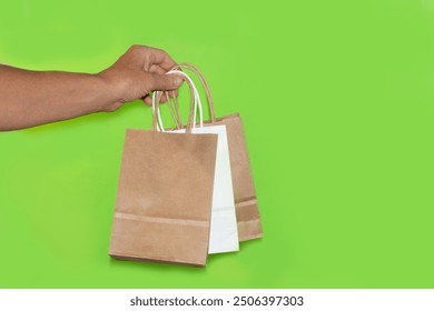 A hand holding two paper shopping bags on a plain background. Eco-friendly packaging. Shopping, product delivery. Gift - Powered by Shutterstock