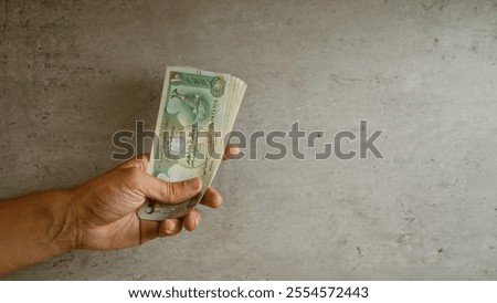 Hand holding uae dirham banknotes against a concrete background symbolizing finance and economy in the united arab emirates