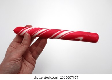 Hand holding unwrapped red and white peppermint polkagris stick candy cane sugar vintage candy bar roll on white background