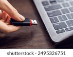 Hand holding usb flash drive with connecting to laptop at wooden table