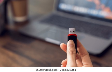 Hand holding usb flash drive with connecting to laptop at wooden table
