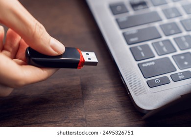 Hand holding usb flash drive with connecting to laptop at wooden table