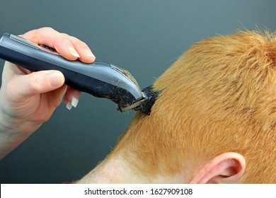 A Hand Holding And Using Hair Clippers To Cut And Trim Ginger Hair.