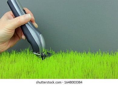 A Hand Holding And Using Hair Clippers To Trim Grass.