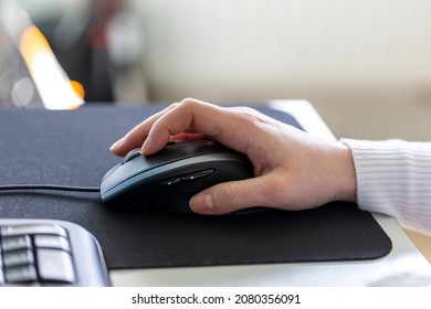 A hand holding and using an optical computer mouse to navigate on screen. The peripheral device is moved around on a mousepad to scroll or browse through applications or internet websites.