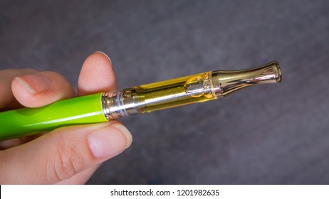 Hand holding a vape pen up close. Cartridge filled with potent THC/CBD cannabis oil.