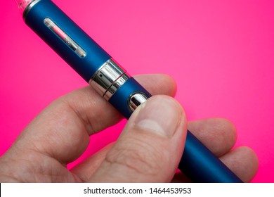 Hand Holding Vape Pen Metal Electronic Cigarette With Vaping Pink Background