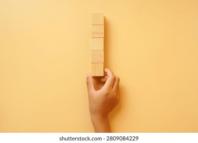 Hand holding a vertical stack of blank wooden blocks on a bright background. Concept of creativity, planning, customization, business strategy, education and copy space.