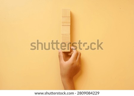 Hand holding a vertical stack of blank wooden blocks on a bright background. Concept of creativity, planning, customization, business strategy, education and copy space.
