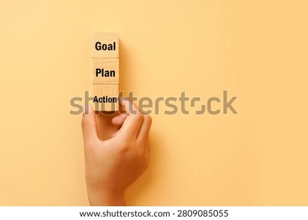 Hand holding a vertical stack of wooden blocks labeled Goal, Plan and Action on a bright background. Concept of strategic planning, goal achievement, execution and personal growth.