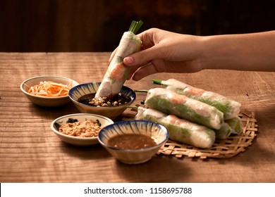 Hand Holding Vietnamese Spring Roll Above The Bowl With Dipping Soy Sauce