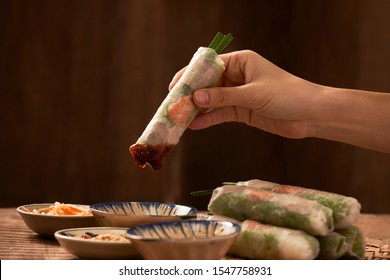 Hand Holding Vietnamese Spring Roll Above The Bowl With Dipping Soy Sauce