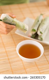 Hand Holding Vietnamese Spring Roll Above The Bowl With Dipping Sauce