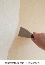 A Hand Holding A Wallpaper Scraper Removing Wallpaper From A Wall 