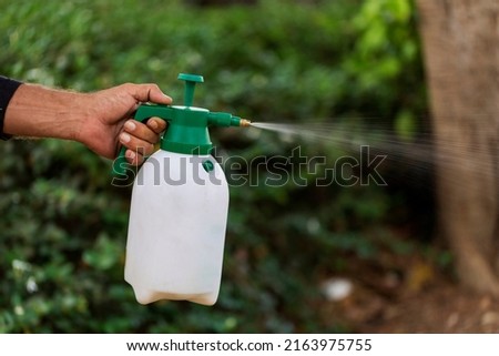 Hand holding watering can and spraying to young plant in garden. Manual sprayer hand pressure pump. Sprayer adjustable nozzle for garden and auto. Sprayer gardening watering pesticide accessories