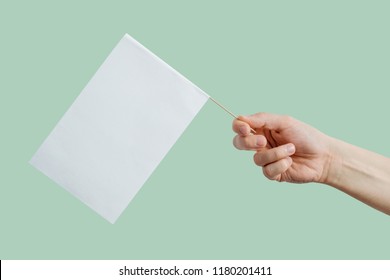 Hand Holding A White, Blank Flag. Content Completion Concept. Blank White Flag Side View. Flag On A Light, Green, Pastel Background.