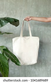 hand holding white blank linen nature canvas tote bag for mock up design. On tropical background