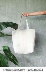hand holding white blank linen nature canvas tote bag for mock up design. On tropical background