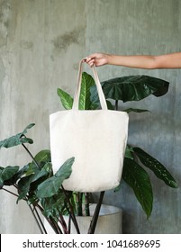 Hand Holding White Blank Linen Nature Canvas Tote Bag For Mock Up Design. On Tropical Background