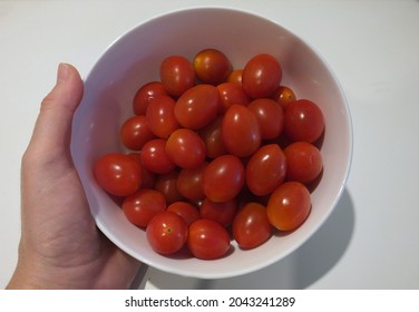 Hand holding a white bowl of cherry tomatoes on a white background