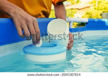 Hand holding white chlorine tablets over swimming pool skimmer. Chlorination of water in pool for disinfection and prevention against the development of microbes.