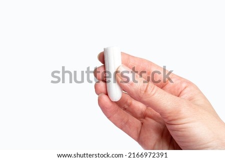 A hand holding a white cotton tampon on a white background. The concept of the menstrual cycle. Women's hygiene and health care. Women's health concept.