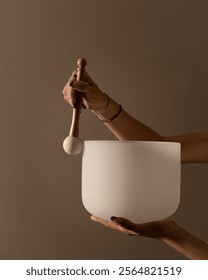 Hand holding a white crystal singing bowl and mallet, creating a serene sound therapy ambiance