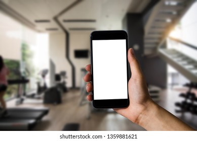 Hand Holding White Mobile Phone With Blank White Screen  In The Gym.