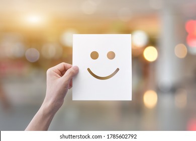 Hand holding white paper and smiley face emoticons (perforated paper) over light bokeh background 
