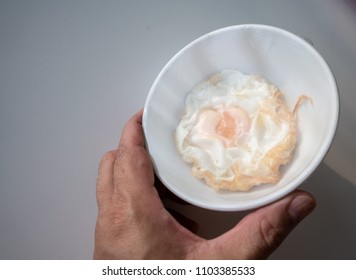 Hand Holding A White Porcelain Bowl Of Fried Egg Covered With Shrink Wrap Film Isolated On White Background. Safety Food Served At Patient Room.