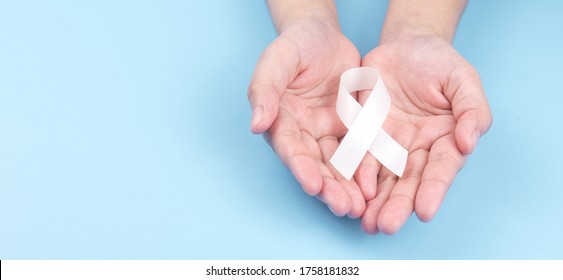 Hand holding white ribbon on blue light color background.
Concept lung cancer awareness November month.
top view.  
copy space.