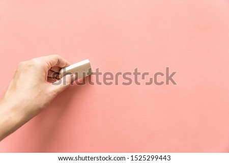 Hand holding white rubber for erasing something on empty pink background. Abstract background with copy space.