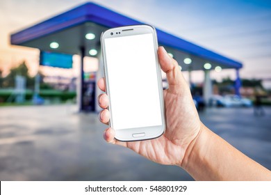 Hand Holding A White Smartphone With Mockup Blank Screen Blur Background Of Twilight Gas Station At Sunset. Touch Screen Mobile Phone At The Petrol Station.