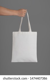 Hand Holding A White Tote Bag Canvas Fabric On Grey Background