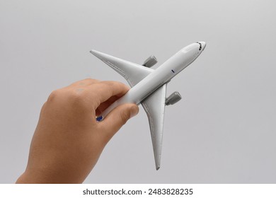 Child’s Hand Holding a White Toy Airplane with Blue Tail Fin on Simple White Background - Powered by Shutterstock