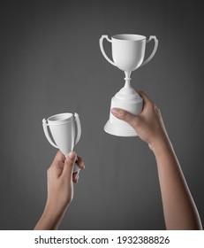 Hand Holding Up White Trophy Cup As A Winner On Grey Concrete Wall