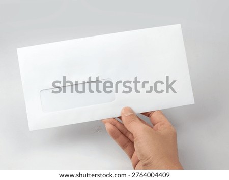 Hand holding white window envelope mockup isolated on gray background. Minimalist stationary template is ideal for showcasing corporate identity designs, official mail, billing statements, and business correspondence.
