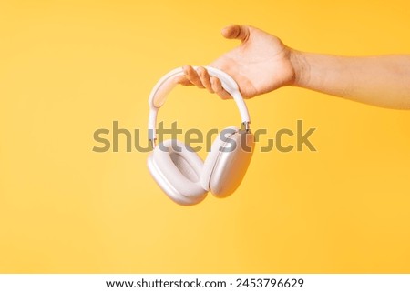 Hand holding white wireless headphones against yellow background.
